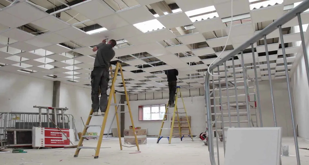 Commercial electrician fitting suspended ceiling lighting on a main contractor fit-out project
