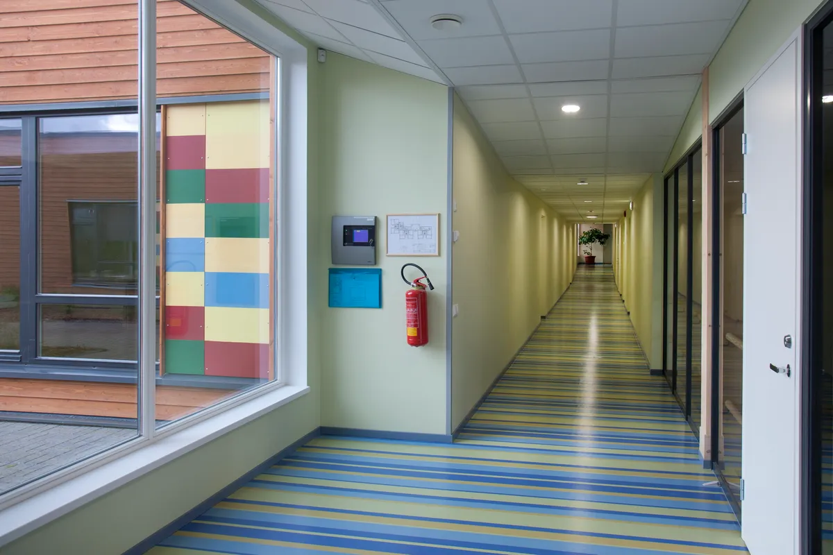 Brightly lit modern school corridor with LED panel lighting, fire alarm panel and emergency-lighting fittings installed by Martin Day Commercial Electricians